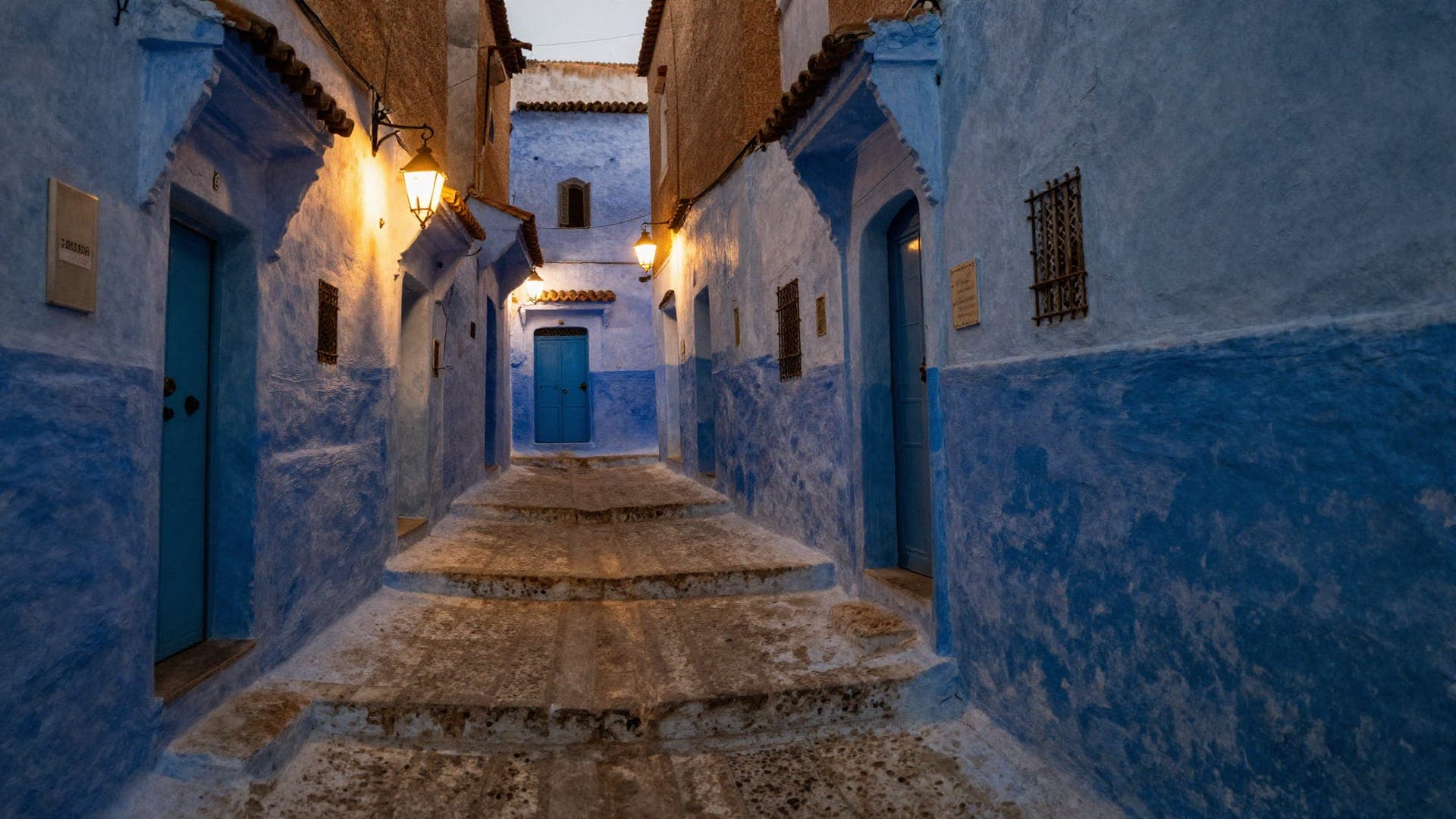 A stepped alley in Chefchaouen washed in blue lime, lanterns lit at dusk, a painted blue door at the top of the steps.